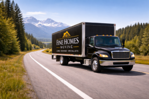 Black moving truck driving on the highway with the words Fine Homes Moving written on it. Mountains are in the background surrounded by green trees